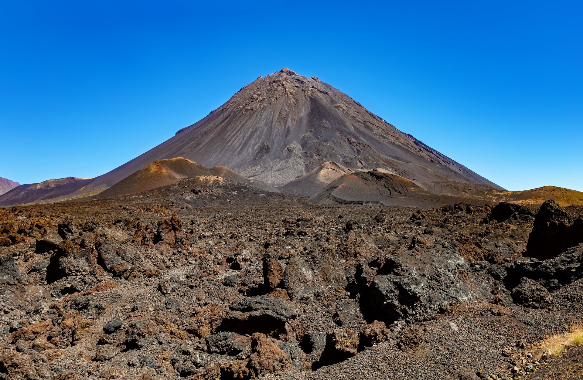 The welcome sign for Parque Natural do Fogo, with the volcanic peak of Pico do Fogo rising in the background at Chã das Caldeiras.