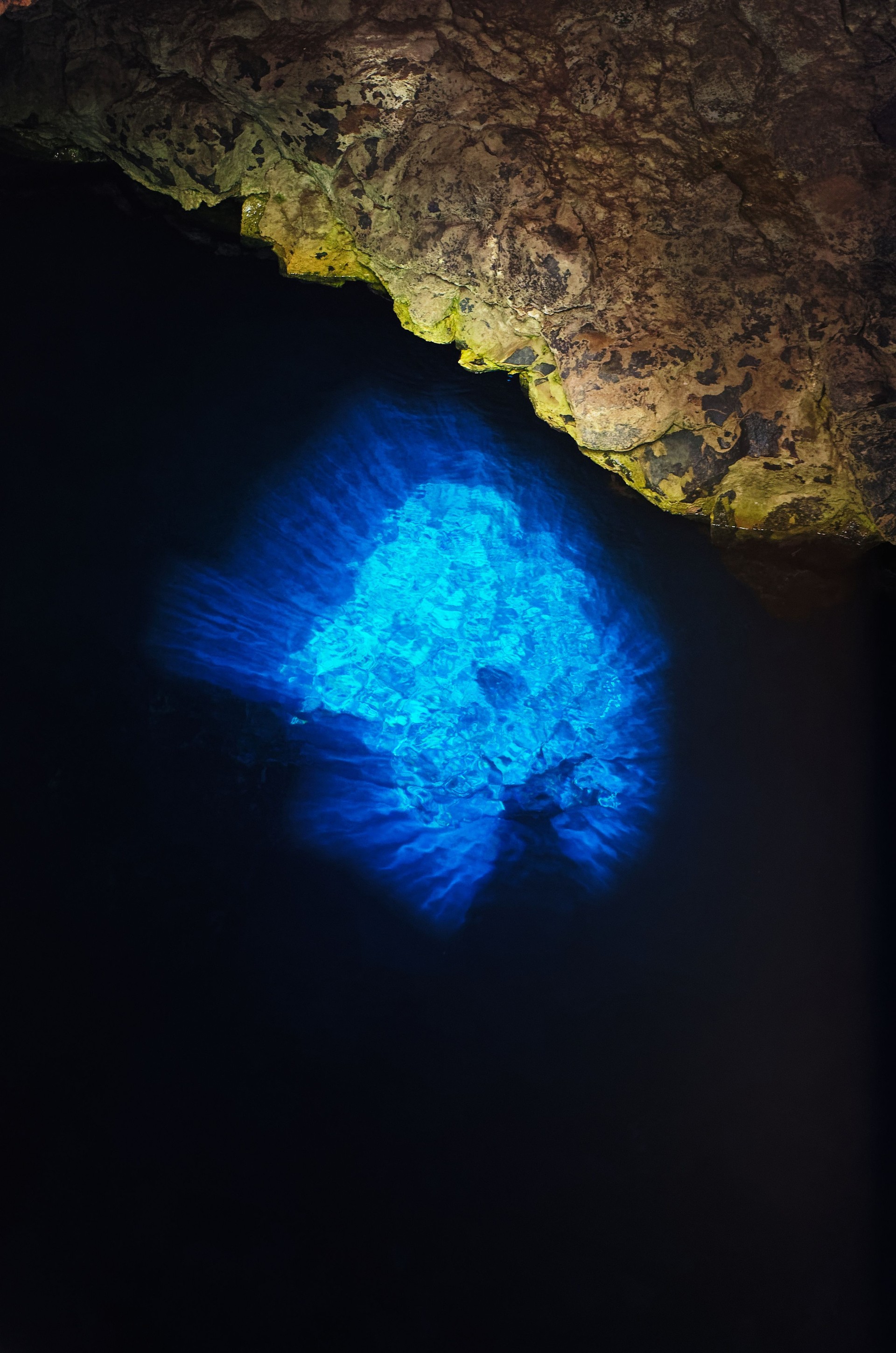 The magical 'Blue Eye' of Buracona on Sal island, glowing an intense turquoise blue as sunlight hits the water inside a natural lava cave.